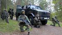 Niederländische und deutsche Soldaten knien vor und neben einem gepanzerten Radfahrzeug.