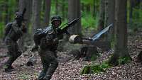 Zwei Soldaten sprinten mit der Waffe im Hochanschlag durch einen Wald.
