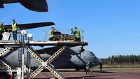 Eine Hebebühne vor einem Flugzeug mit einem Patienten auf einer Bahre und Soldaten.