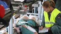 Eine deutsche Soldatin spricht mit einer Patientin auf einer Trage und notiert etwas.