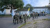 Soldaten mit zwei Fahnenträgern laufen durch ein Kasernentor