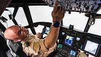 Ein Soldat sitzt in einem Cockpit und betätigt einen Schalter.