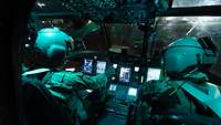 Zwei Piloten sitzen bei Nacht im Cockpit eines Hubschraubers.
