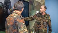 Zwei Soldaten stehen sich gegenüber und sprechen, einer zeigt auf ein Foto auf einem Monitor.