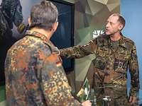 Zwei Soldaten stehen sich gegenüber und sprechen, einer zeigt auf ein Foto auf einem Monitor.