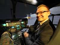 Ein Mann mit Brille sitzt in einem Cockpit. Im Hintergrund ist eine Mondlandschaft zu sehen.