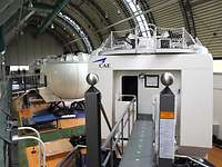 Mehrere große, weiße kugelförmige Simulatoren mit Verbindungswegen befinden sich in einer Halle.