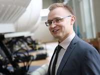 Portätfoto eines Mannes mit Brille. Der Hintergrund zeigt unscharf mehrere große weiße Simulatoren.