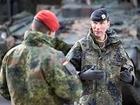 Zwei Soldaten stehen sich gegenüber und sprechen miteinander. Im Hintergrund steht ein Panzer.