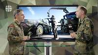 Zwei Soldaten stehen sich an einem Tisch gegenüber und sprechen, hinter ihnen ein Monitor mit Foto.