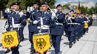 Soldaten mit Musikinstrumenten marschieren über einen Platz.
