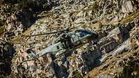 Ein Hubschrauber fliegt vor einer Felswand im Gebirge.