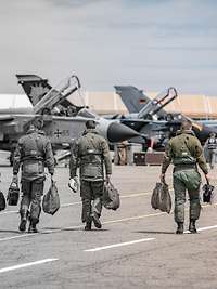 Vier Piloten laufen zu ihren Maschinen. Von Rechts nach Links verschwindet die Farbe.