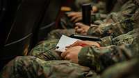 Mehrere Soldaten sitzen nebeneinander mit Schreibutensilien während eines Vortrags.