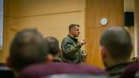 Ein stehender Soldat spricht zu sitzenden Soldaten in einem Hörsaal.