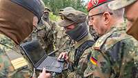 Mehrere Soldaten stehen zusammen im Gelände und schauen gemeinsam auf einen Laptop.