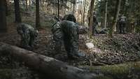 Mehrere Soldaten heben mit Klappspaten im Wald Stellungen aus.