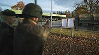 Zwei Soldaten stehen auf einer Wiese vor einer Schützenscheibe, im Hintergrund ein Fahrzeug.