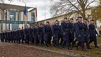 Mehrere Soldaten marschieren in zwei Reihen vor einem Gebäude.