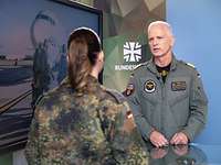 Eine Soldatin und ein Soldat stehen sich gegenüber. Neben ihnen steht ein großer Monitor.