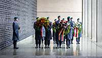 Soldaten tragen große Kränze in das Ehrenmal der Bundeswehr. Ein Soldat mit Trompete steht daneben.