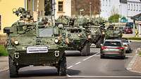 Several military vehicles pass through a small town.