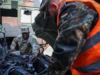 Two soldiers repair a vehicle.