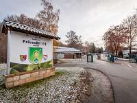 Ein Schild des Bataillons, dahinter die Wache und die Einfahrt mit Schlagbäumen und einem Zaun