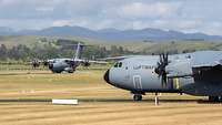 Zwei Transportflugzeuge rollen auf der Start- und Landebahn. Im Hintergrund eine bergige Landschaft.