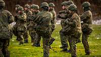 Eine Gruppe von Soldaten in Uniform macht Sport auf einer Wiese.