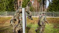 Mehrere Soldaten überwinden auf einer Rasenfläche eine Holzwand.