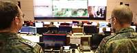Zwei Soldaten stehen in einem großen Raum vor Monitoren