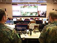 Zwei Soldaten stehen in einem großen Raum vor Monitoren