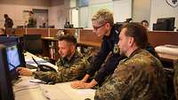 Zwei Soldaten und eine Polizisten schauen auf einen Monitor