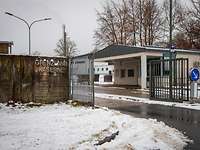 Einfahrt mit Steinmauer und Metallzaun, rechts das flache Wachgebäude.