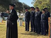 Ein Pfarrer hält eine Andacht, im Hintergrund stehen Soldaten.