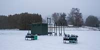 Ein grüner Container im Schnee mit Klimmzugstangen und zwei Hantelständern im Vordergrund