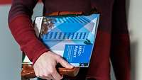 Eine Person hält eine Broschüre mit dem Titel MAD-Report in der Hand.
