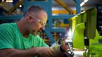 Ein Mann mit Schutzbrille arbeitet an einem gelb grundierten Metallstück.
