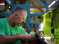 Ein Mann mit Schutzbrille arbeitet an einem gelb grundierten Metallstück.