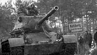 Schwarz-Weiß-Aufnahme: Soldaten fahren in einem Panzer an dem Ortsschild Kohlberg vorbei.