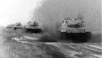 Schwarz-Weiß-Aufnahme: Mehrere Panzer fahren hintereinander im Gelände.