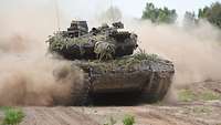 Ein Panzer fährt im Gelände und wirbelt Staub auf.