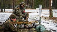 Eine Soldatin liegt auf einer Tarndecke hinter einem Maschinengewehr, der Ausbilder hockt daneben.
