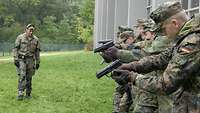 Soldaten stehen auf einer Wiese mit einer Pistole in der Hand, ein Ausbilder steht vor ihnen.