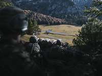 Im Wald am Berghang liegen Soldaten mit Gewehren in Stellung und schauen ins Tal.