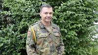 Ein Soldat steht vor einer grünen Hecke