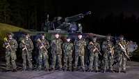 Mehrere Soldaten stehen nachts auf einem dunklen Platz mit Waffen vor einem Panzer.