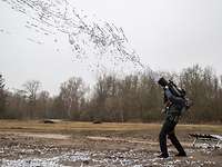 Ein maskierter Mann feuert eine Kanone auf seiner Schulter ab. Silberne Fäden fliegen heraus.