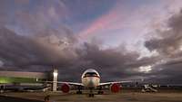 Ein Flugzeug in Frontalansicht steht auf einem Flugplatz. Am Himmel ist eine Wolkendecke zu sehen.